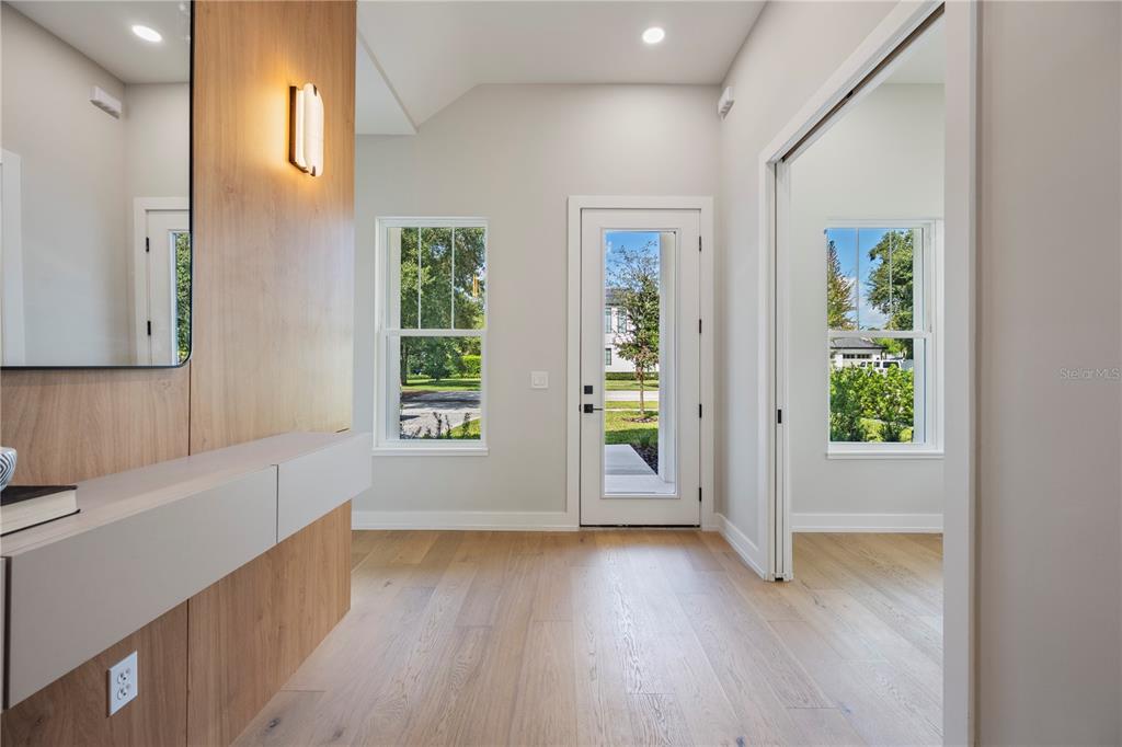 A bright entryway features light wood flooring, a wood-paneled wall, a mirror, and a glass door — 1702 ARBOR PARK DRIVE, WINTER PARK, FL