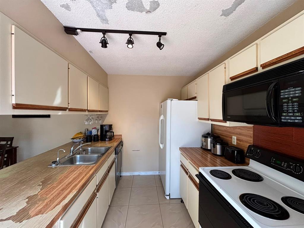 A galley kitchen features light-colored cabinets, wood-look laminate countertops, and a white refrigerator — 5277 CORAL COURT UNIT 625, ORLANDO, FL
