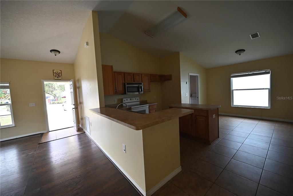 An open-concept kitchen with wood cabinets and a breakfast bar overlooks a tiled living area — 5302 SCHOOL ROAD, NEW PORT RICHEY, FL