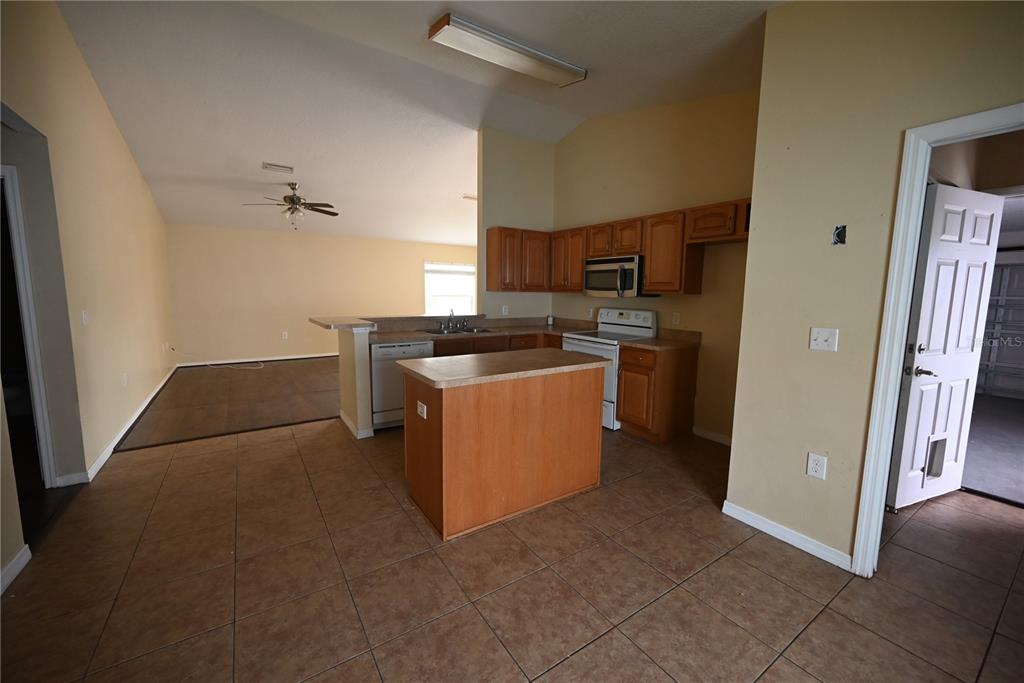A kitchen with wood cabinets, a center island, and tile flooring opens to a living area — 5302 SCHOOL ROAD, NEW PORT RICHEY, FL