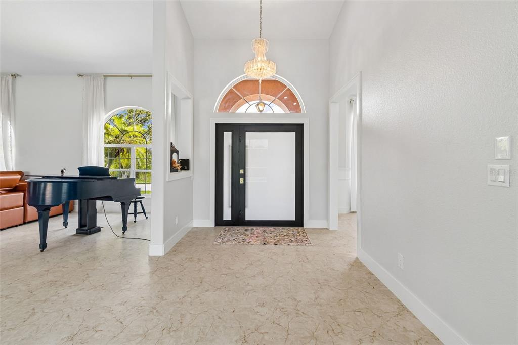 A bright entryway features a black front door, a crystal chandelier, and marble-look flooring — 3339 DESOTO DRIVE, PUNTA GORDA, FL