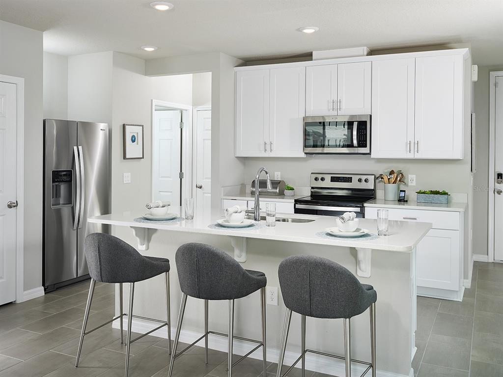 A modern kitchen features white cabinetry, stainless steel appliances, and a breakfast bar with stools — 4531 RANGELAND WAY, ST CLOUD, FL