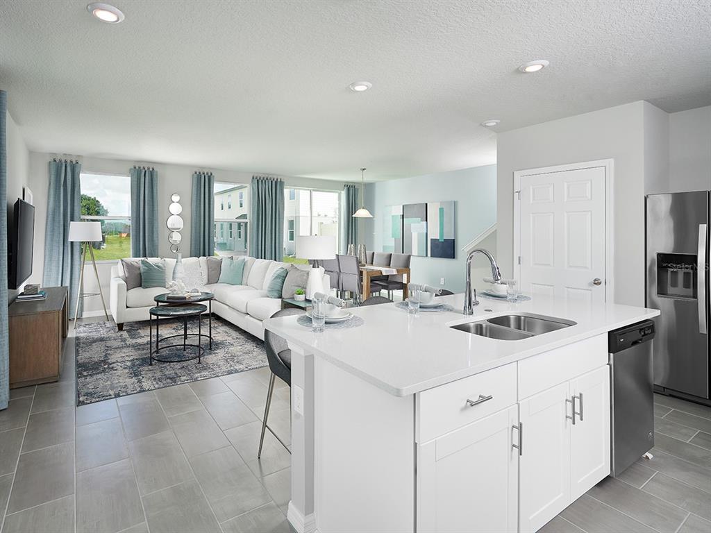 A bright open-concept kitchen and living area featuring white cabinetry, quartz countertops, and tile flooring — 4531 RANGELAND WAY, ST CLOUD, FL