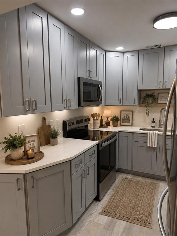 A kitchen features gray shaker cabinets, white countertops, stainless steel appliances, and light wood flooring — 8080 112TH STREET UNIT 107, SEMINOLE, FL
