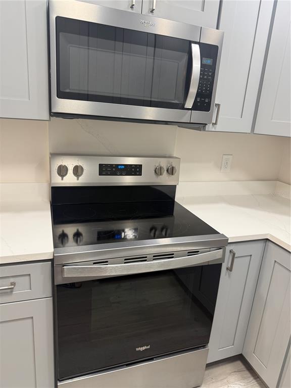 A stainless steel microwave and electric range are installed between light gray kitchen cabinets — 8080 112TH STREET UNIT 107, SEMINOLE, FL