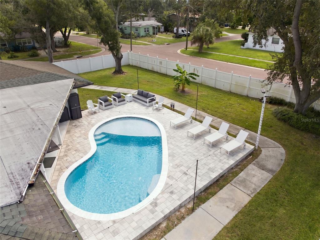 An aerial view of a backyard featuring a kidney-shaped pool, patio furniture, and white fencing — 330 PATICA RD NE, ST PETERSBURG, FL