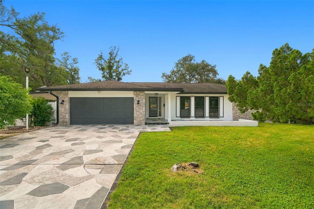A single-story house with a stone-accented facade, a two-car garage, and a patterned concrete driveway — 330 PATICA RD NE, ST PETERSBURG, FL