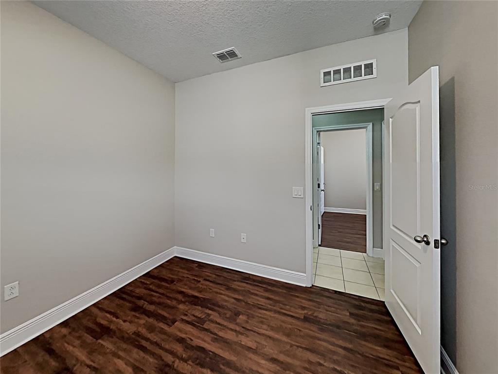 An empty room features wood-look flooring, light gray walls, and an open doorway to a hallway — 7033 FEATHER WOOD DR, RUSKIN, FL