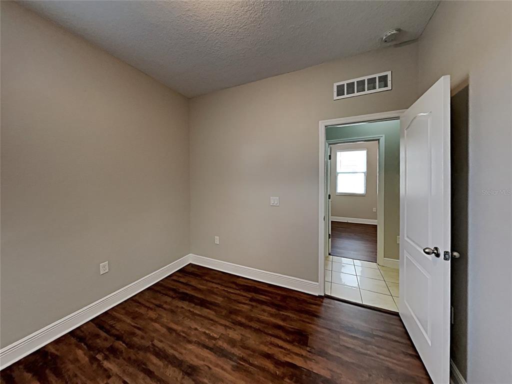 An empty room features wood-look flooring, light gray walls, and an open doorway to another room — 7033 FEATHER WOOD DR, RUSKIN, FL