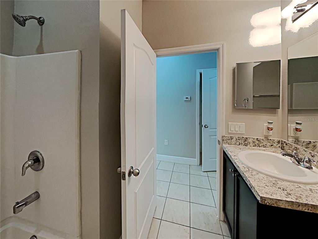 A bathroom features a shower-tub combination, a dark vanity with a granite countertop, and tile flooring — 7033 FEATHER WOOD DR, RUSKIN, FL