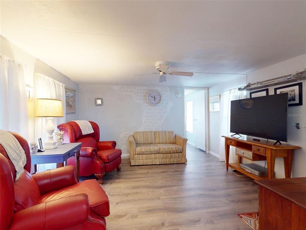 A living room features wood-look flooring, a ceiling fan, a television console, and a red chair — 2201 S RIDGEWOOD AVENUE UNIT 8, EDGEWATER, FL
