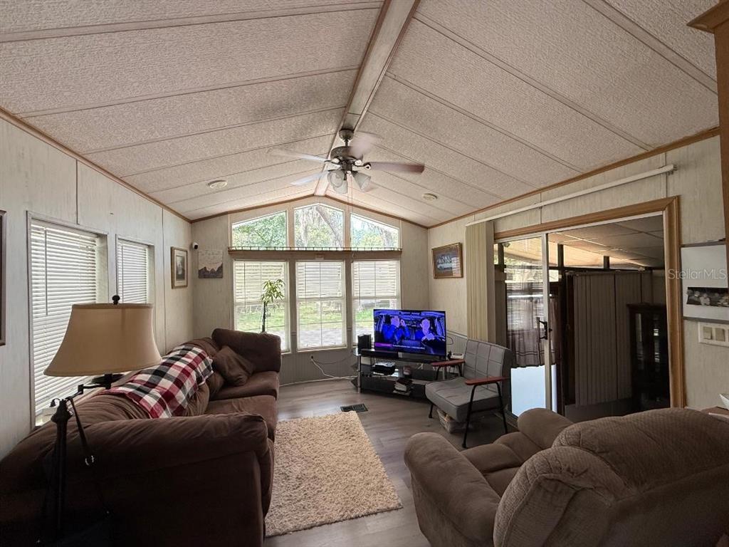 A living room with a vaulted ceiling, ceiling fan, brown furniture, and large windows — 3000 CLARCONA ROAD UNIT 423, APOPKA, FL