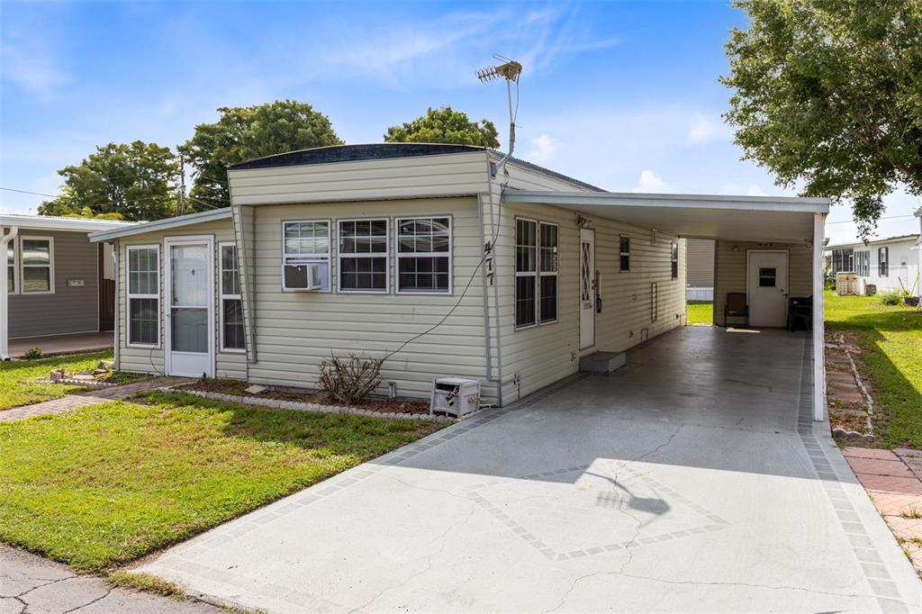 A light-colored mobile home with a carport, driveway, and small front lawn — 477 MARINA LANE, TAVARES, FL