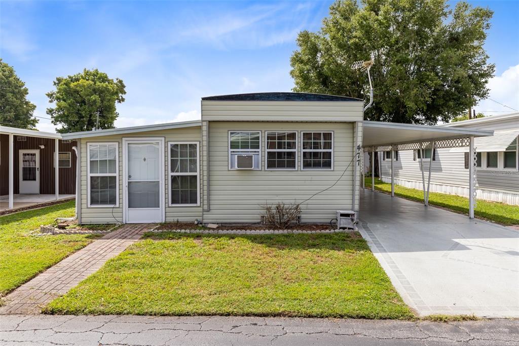 A single-story mobile home with light siding, a front walkway, and an attached carport — 477 MARINA LANE, TAVARES, FL