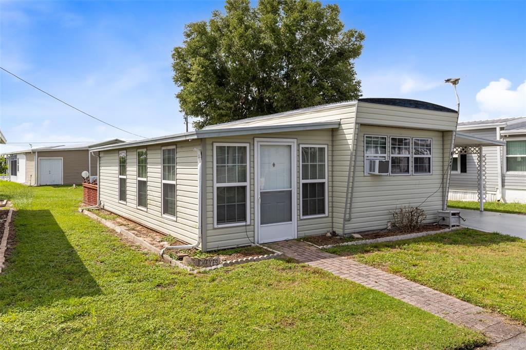 A light-colored mobile home with a brick walkway and a large tree in the background — 477 MARINA LANE, TAVARES, FL
