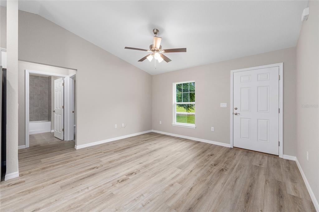 An empty room with light wood-look flooring, a ceiling fan, and a door to a bathroom — 21812 SW RAINBOW LAKES BOULEVARD, DUNNELLON, FL