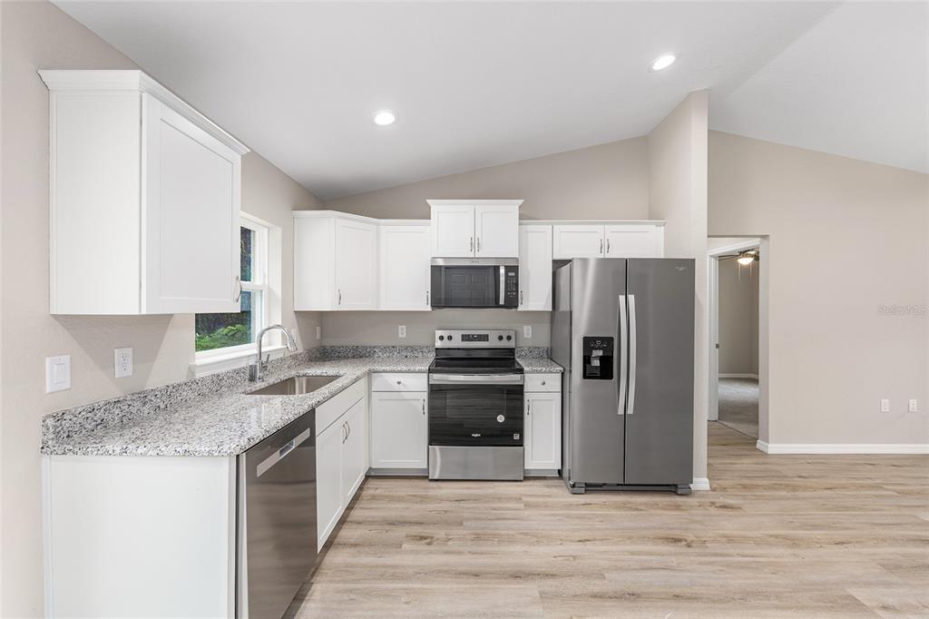 A kitchen with white cabinets, granite countertops, stainless steel appliances, and light wood-look flooring — 21812 SW RAINBOW LAKES BOULEVARD, DUNNELLON, FL