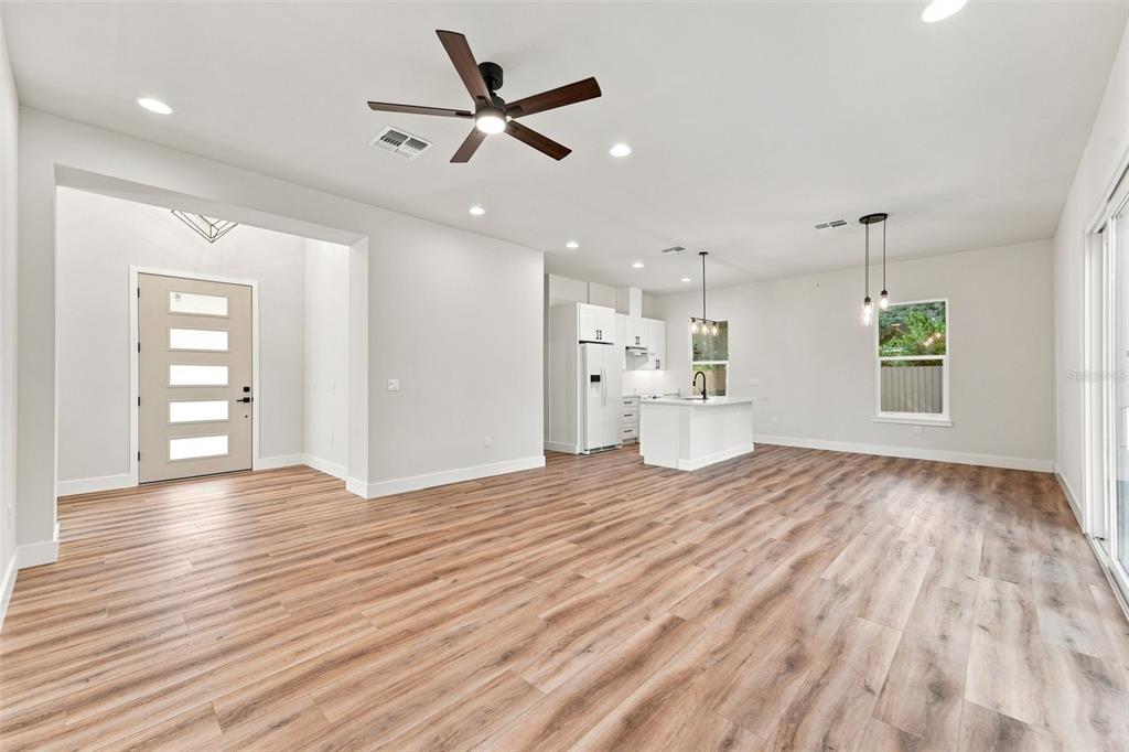 An open-concept living area features light wood-look flooring, a ceiling fan, and a white kitchen — 561 N THOMPSON ROAD, APOPKA, FL