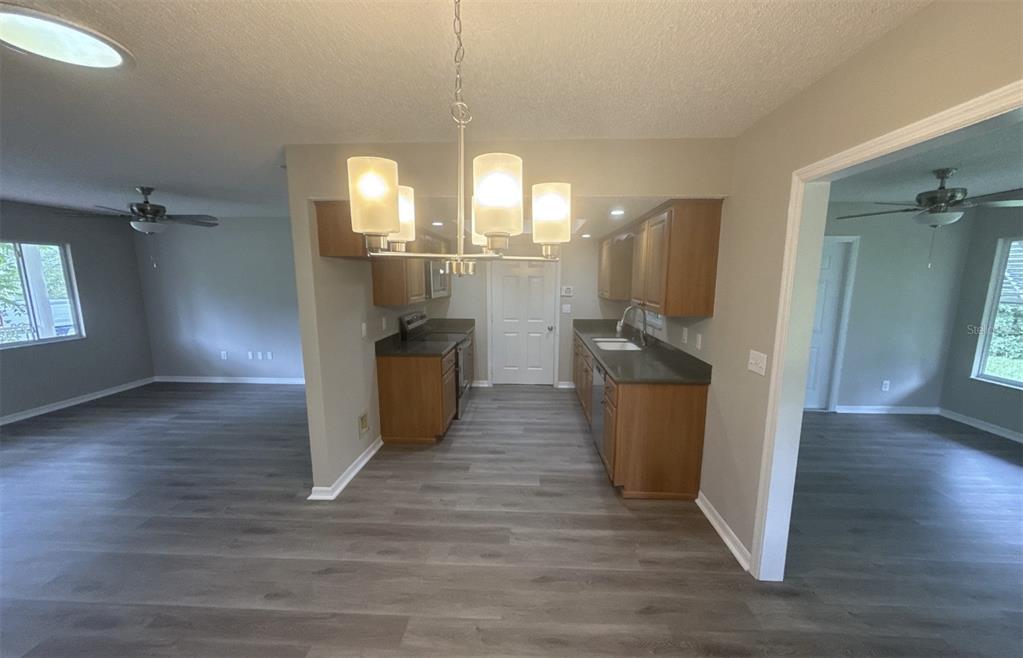 A kitchen with wood cabinets and dark countertops sits between two living areas with flooring — 17655 SE 102ND CIRCLE, SUMMERFIELD, FL