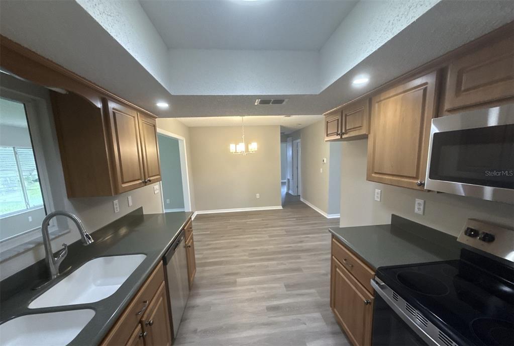A kitchen with wood cabinets, gray countertops, and stainless steel appliances opens into a dining area — 17655 SE 102ND CIRCLE, SUMMERFIELD, FL