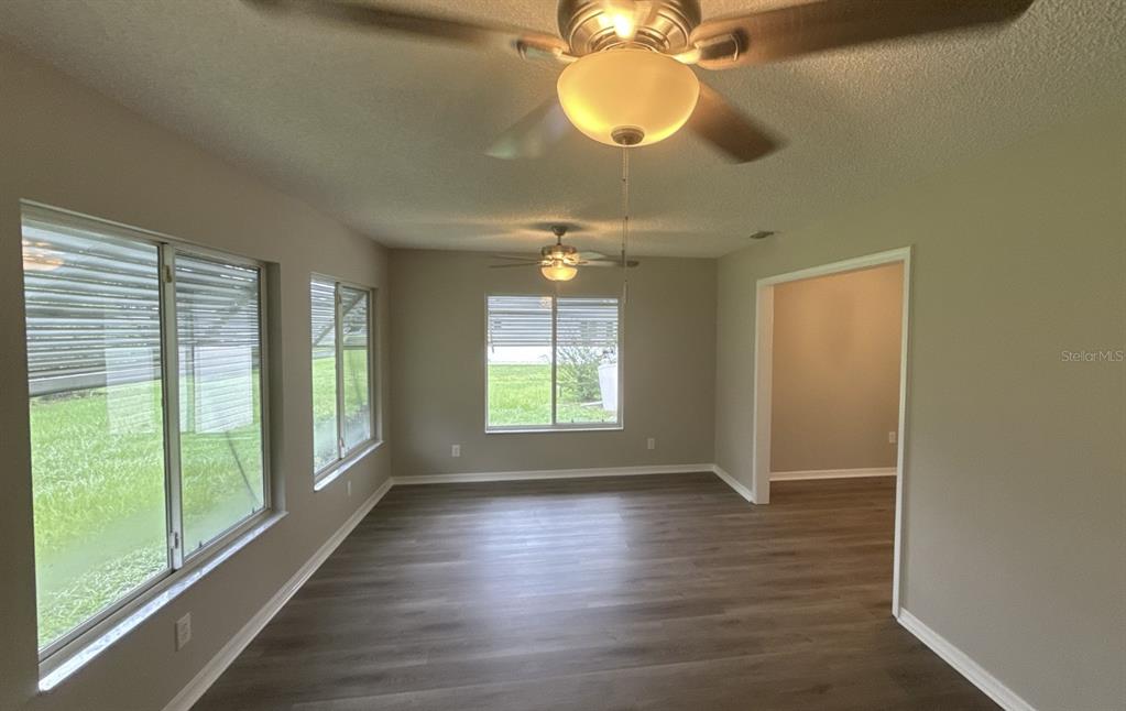 An empty room features wood-look flooring, two ceiling fans, and multiple windows overlooking a yard — 17655 SE 102ND CIRCLE, SUMMERFIELD, FL