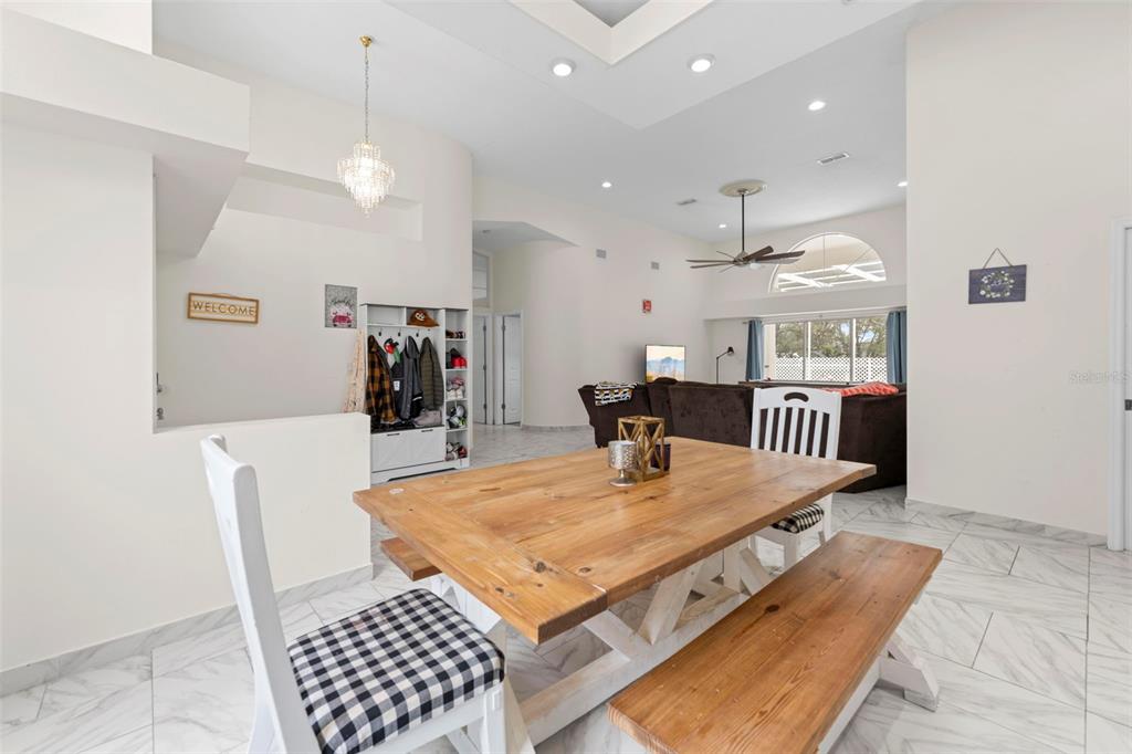 A dining area with a wooden table and bench overlooks a living room with tile floors — 348 FLORIAN WAY, SPRING HILL, FL