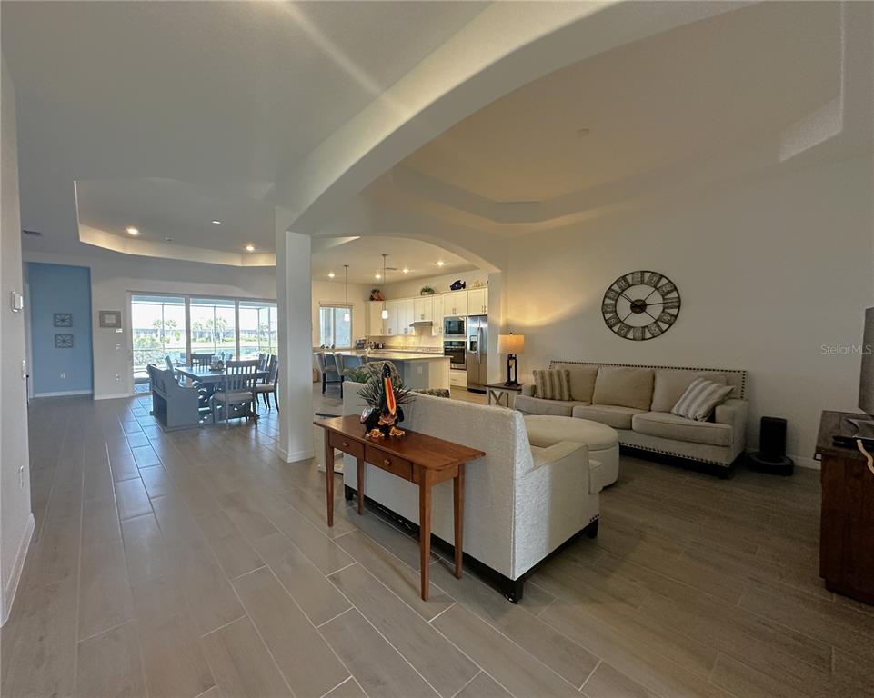 An open-concept living room and kitchen area features tile flooring and a large wall clock — 15172 RIVER BIRCH COURT, PUNTA GORDA, FL