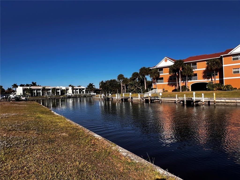 A canal runs between a grassy bank and a multi-story orange apartment building with docks — 1443 MEDITERRANEAN DRIVE, PUNTA GORDA, FL