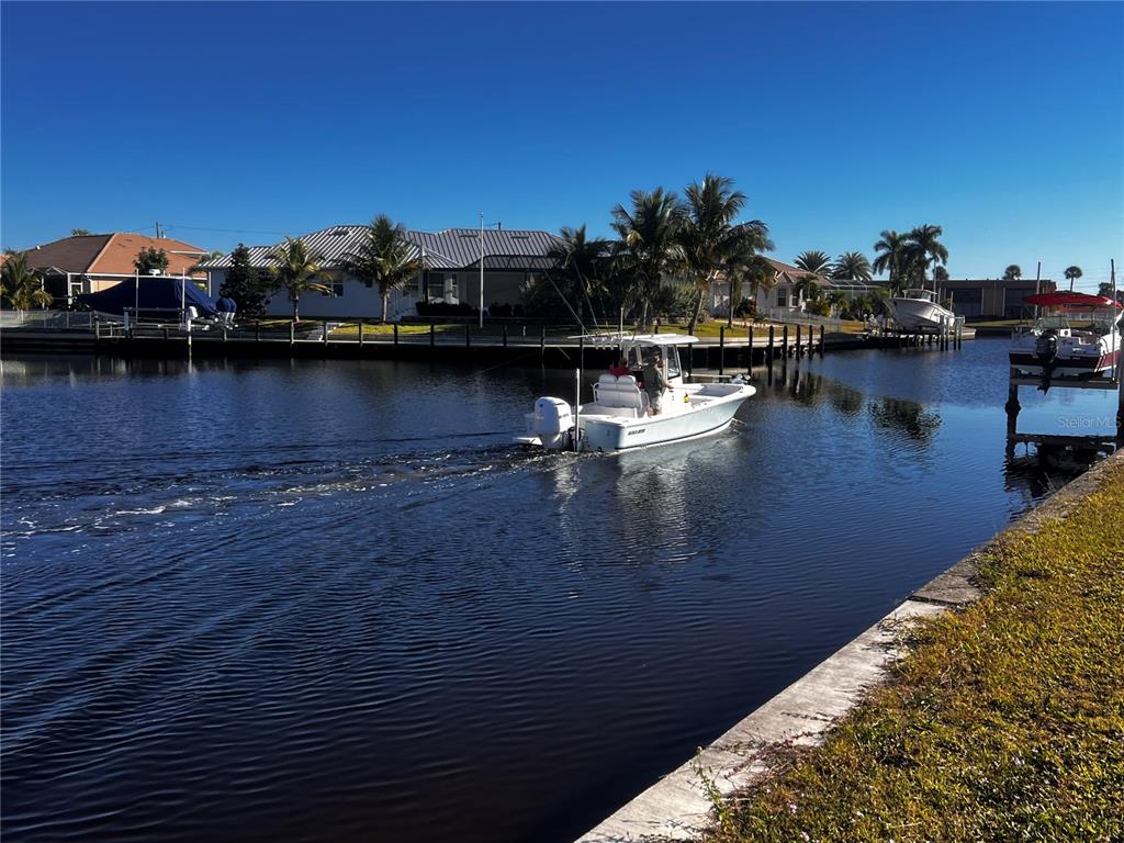 A white motorboat travels down a canal past waterfront houses and palm trees — 1443 MEDITERRANEAN DRIVE, PUNTA GORDA, FL