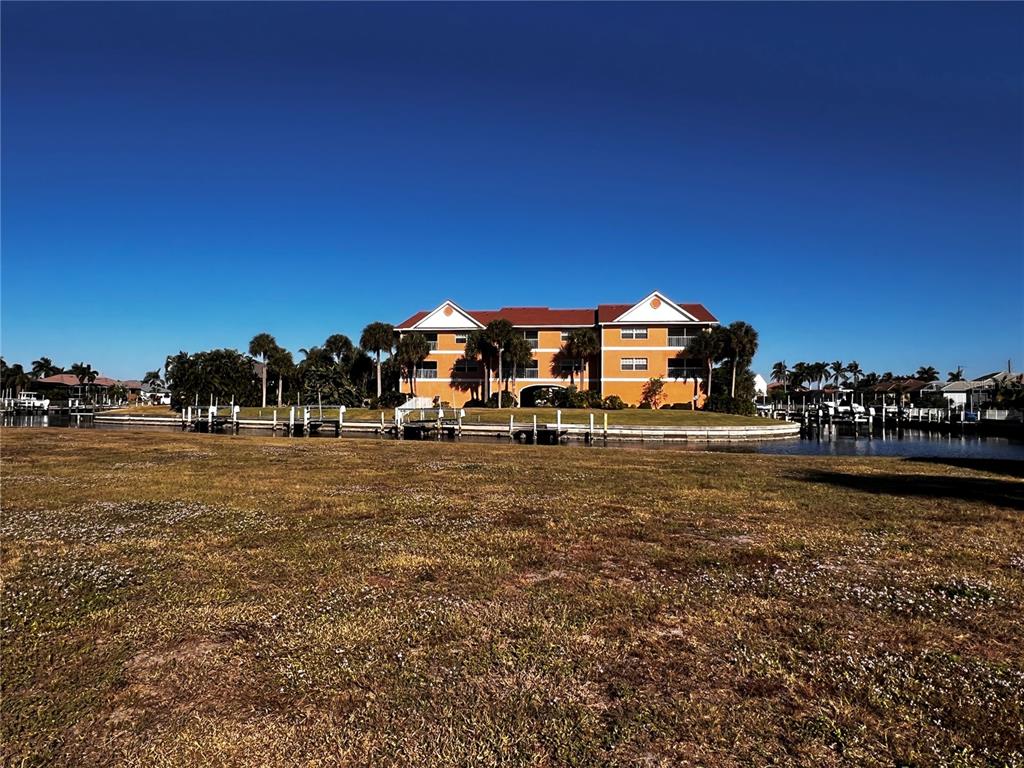 An orange multi-story building sits behind a grassy field and a canal with boat docks — 1443 MEDITERRANEAN DRIVE, PUNTA GORDA, FL