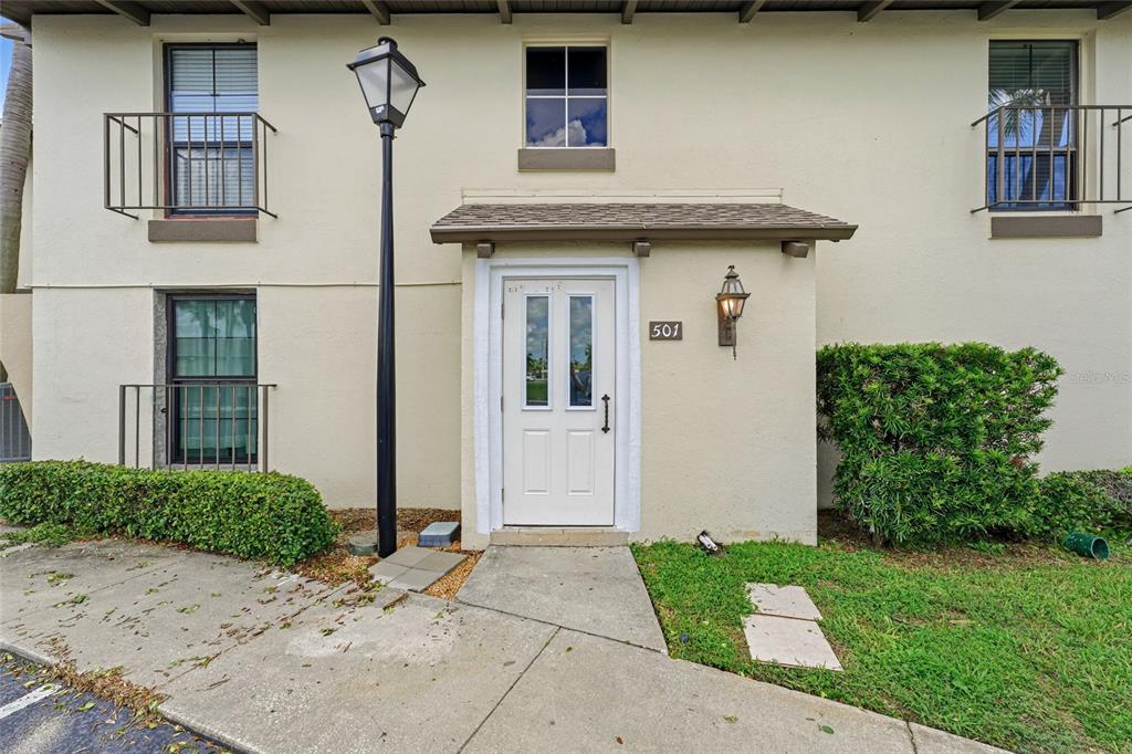 The exterior of a two-story residential building features a white front door labeled 501 — 501 PLAZA SEVILLE COURT UNIT 2, TREASURE ISLAND, FL