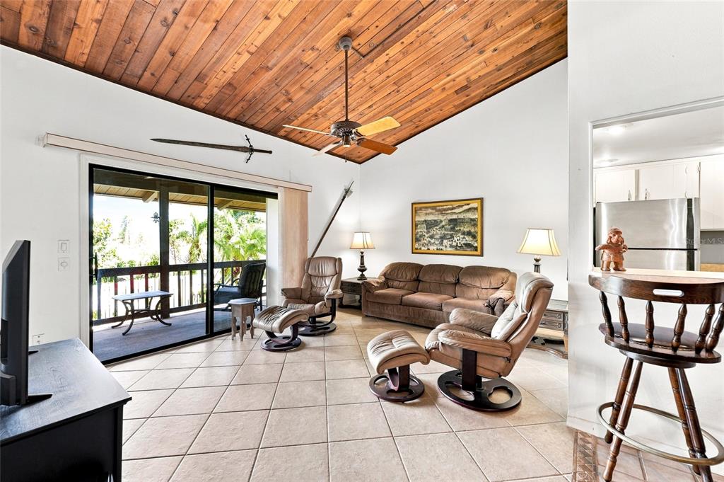 A living room features a wood-plank vaulted ceiling, tile flooring, and a sliding glass door — 501 PLAZA SEVILLE COURT UNIT 2, TREASURE ISLAND, FL