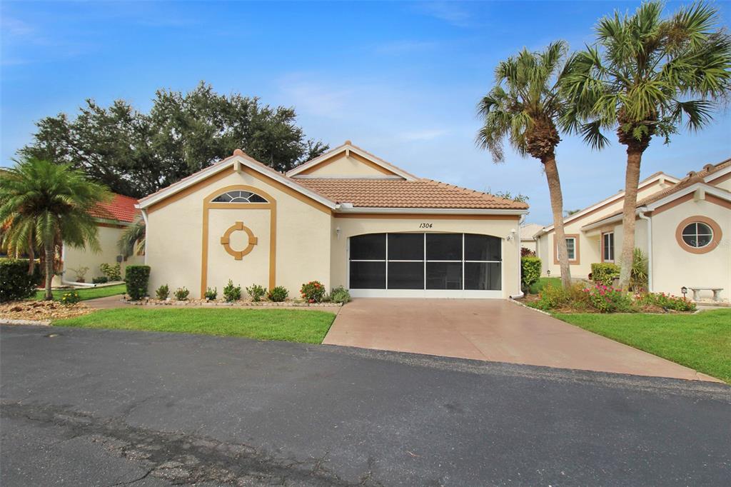 A single-story house with a beige stucco exterior, a screened garage, and two palm trees — 1304 CAPRI ISLES BOULEVARD UNIT 31, VENICE, FL