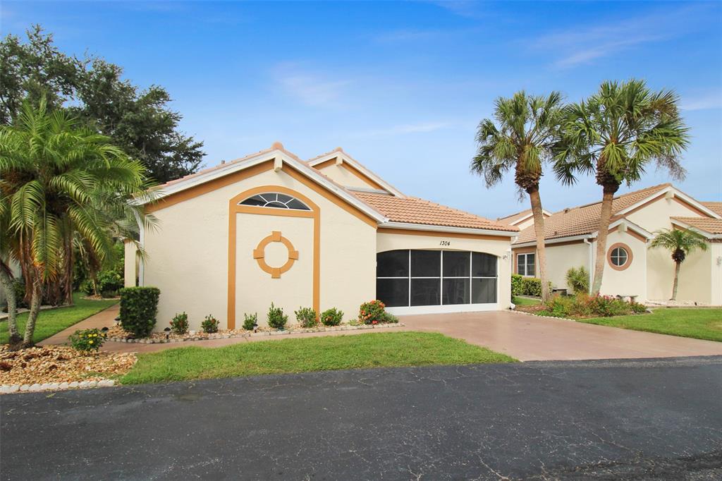 A single-story house with a screened-in garage, tan stucco walls, and two palm trees — 1304 CAPRI ISLES BOULEVARD UNIT 31, VENICE, FL