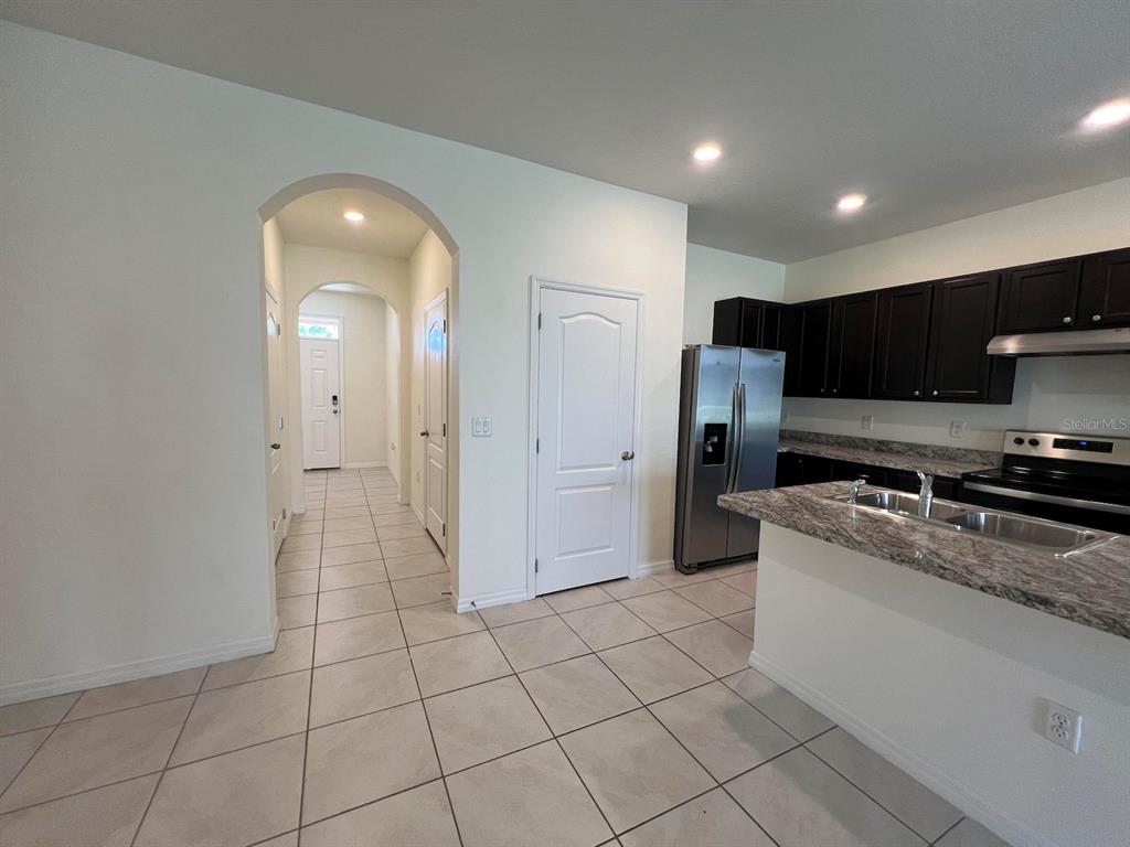 A kitchen with dark cabinets and granite countertops opens to a tiled hallway with arched doorways — 1370 YELLOW FINCH DRIVE, DAVENPORT, FL
