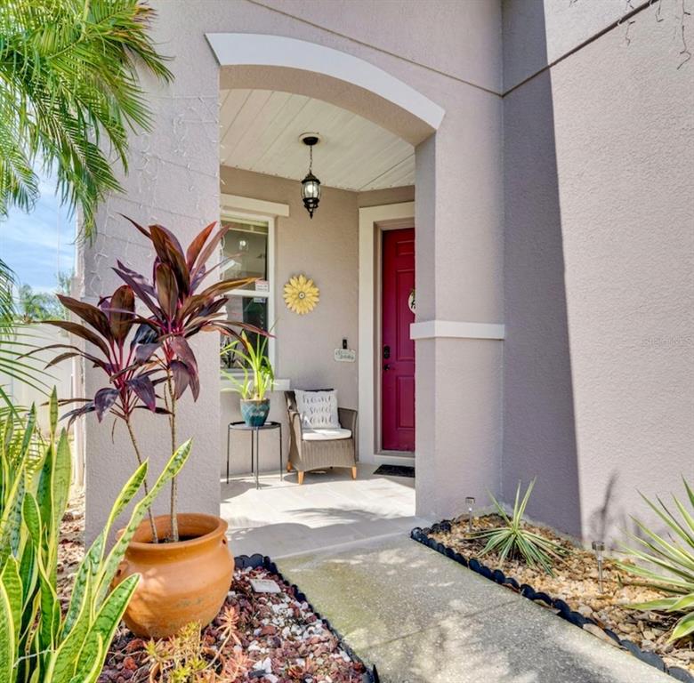 A covered entryway features a red front door, a wicker chair, and potted plants — 345 SONJA CIRCLE, DAVENPORT, FL