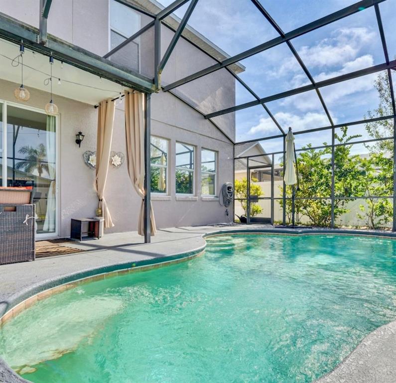 A screened-in patio features a curved swimming pool and beige curtains against a house exterior — 345 SONJA CIRCLE, DAVENPORT, FL