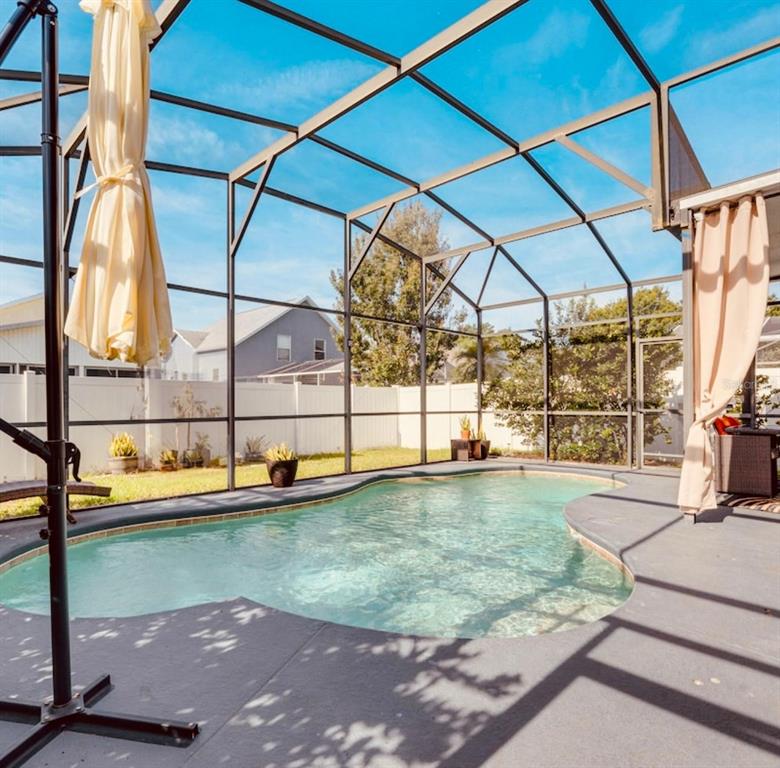 A screened-in swimming pool with a concrete deck and a beige umbrella in a backyard — 345 SONJA CIRCLE, DAVENPORT, FL