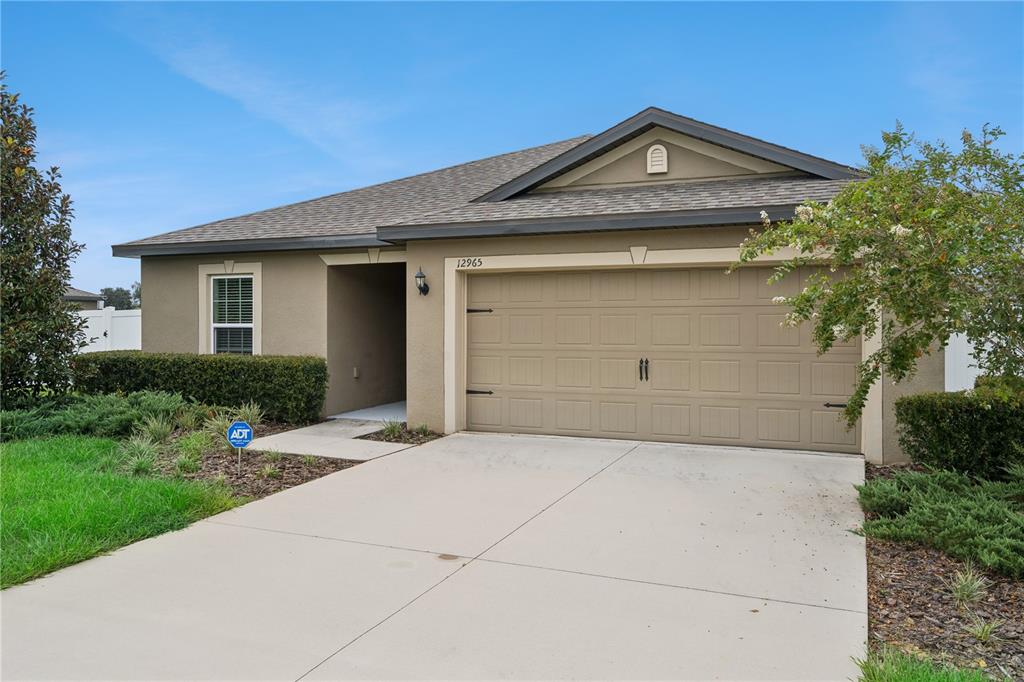 A single-story house with a beige stucco exterior, a two-car garage, and a concrete driveway — 12965 DEL LAGO DRIVE, ASTATULA, FL