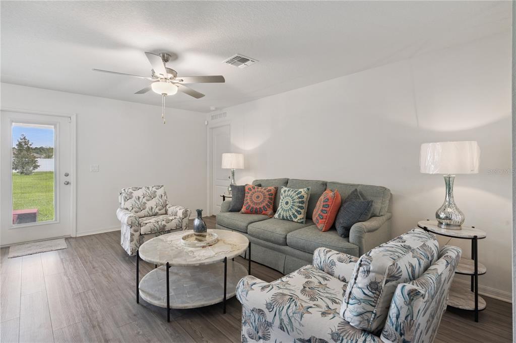 A living room features a gray sofa, two patterned armchairs, and a round coffee table — 12965 DEL LAGO DRIVE, ASTATULA, FL