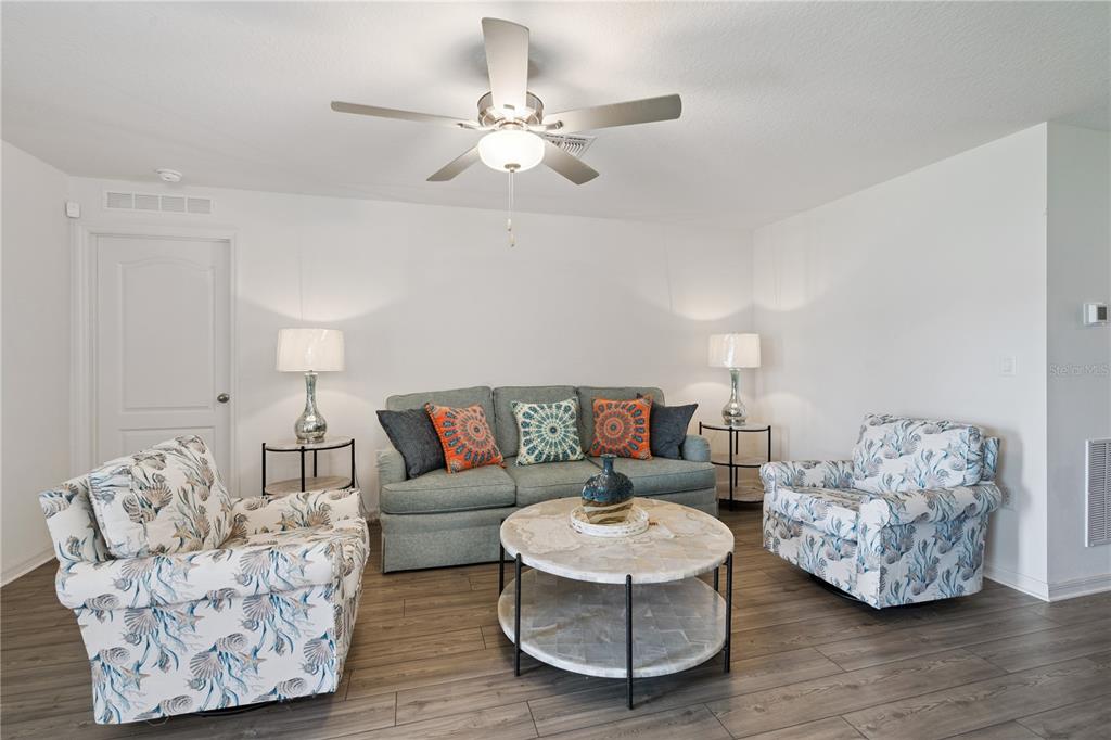A living room features a sofa, two patterned armchairs, a round coffee table, and a fan — 12965 DEL LAGO DRIVE, ASTATULA, FL