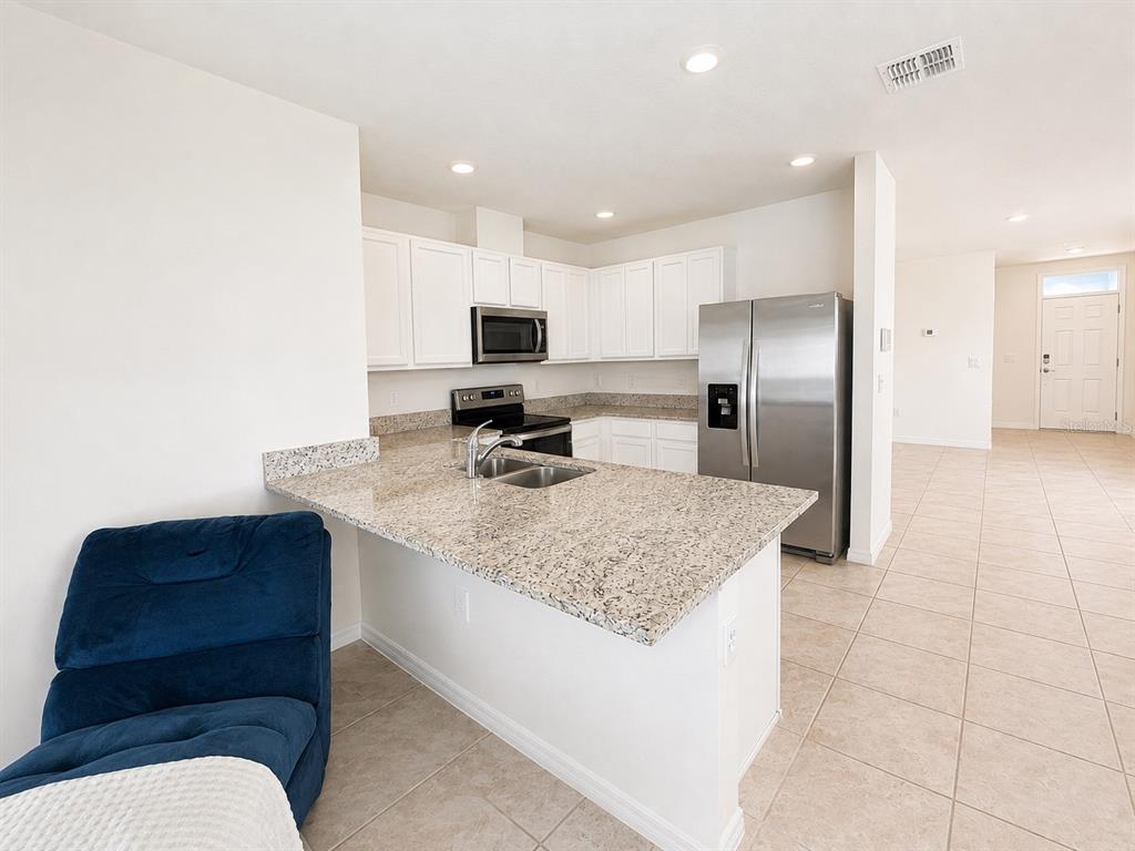 A kitchen with white cabinets, granite countertops, stainless steel appliances, and a blue armchair — 3648 SUNGROVE CIRCLE, SANFORD, FL