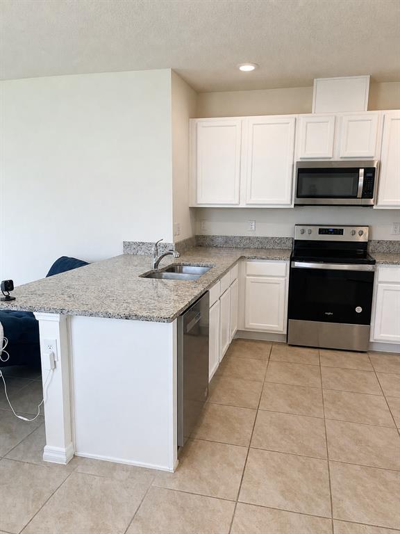 A kitchen features white cabinets, granite countertops, stainless steel appliances, and light-colored tile flooring — 3648 SUNGROVE CIRCLE, SANFORD, FL