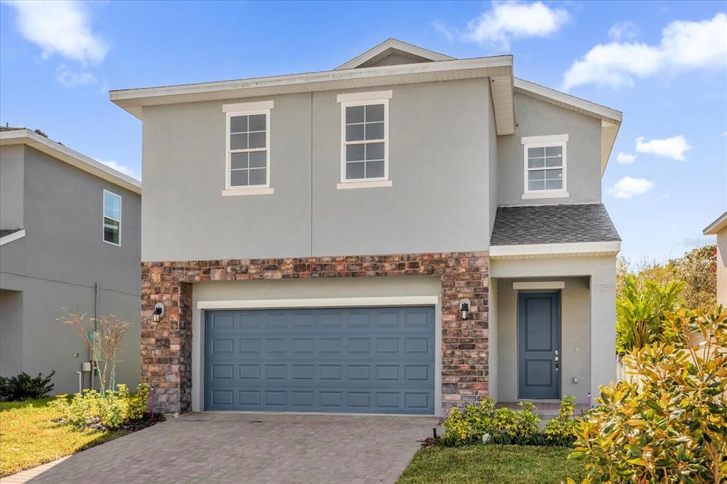 A two-story house with a gray stucco exterior, brick accents, and a blue garage door — 1251 ASH TREE COVE, CASSELBERRY, FL
