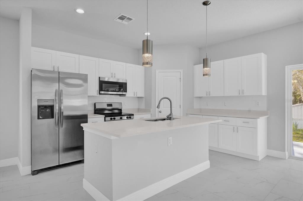A modern kitchen features white cabinetry, stainless steel appliances, a center island, and light flooring — 1251 ASH TREE COVE, CASSELBERRY, FL