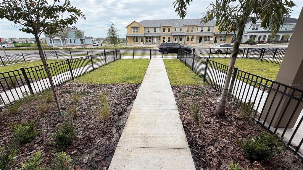 A concrete walkway leads through a fenced yard toward a street with parked cars — 2133 SOUTHBURY DRIVE, KISSIMMEE, FL