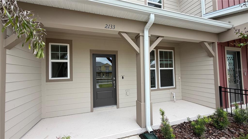 A covered front porch with beige siding, a dark front door, and a white downspout — 2133 SOUTHBURY DRIVE, KISSIMMEE, FL