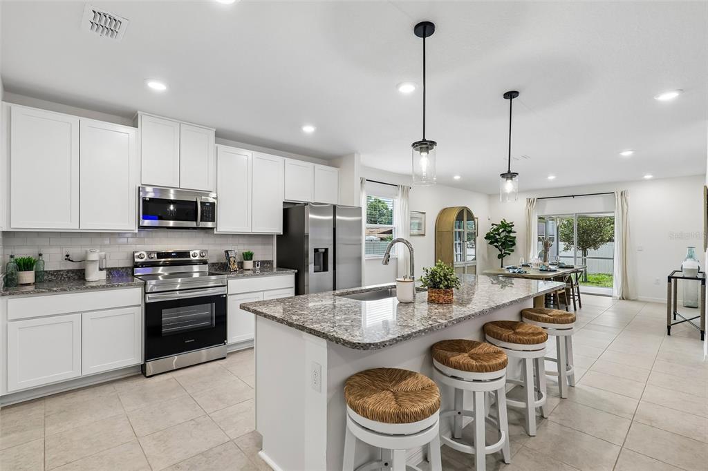 A modern kitchen features white cabinets, granite countertops, a center island with stools, and appliances — 5955 LYON ROAD, SPRING HILL, FL