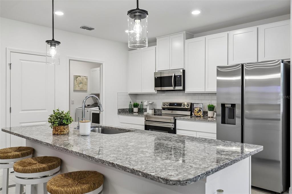 A modern kitchen features white cabinets, granite countertops, stainless steel appliances, and a central island — 5955 LYON ROAD, SPRING HILL, FL