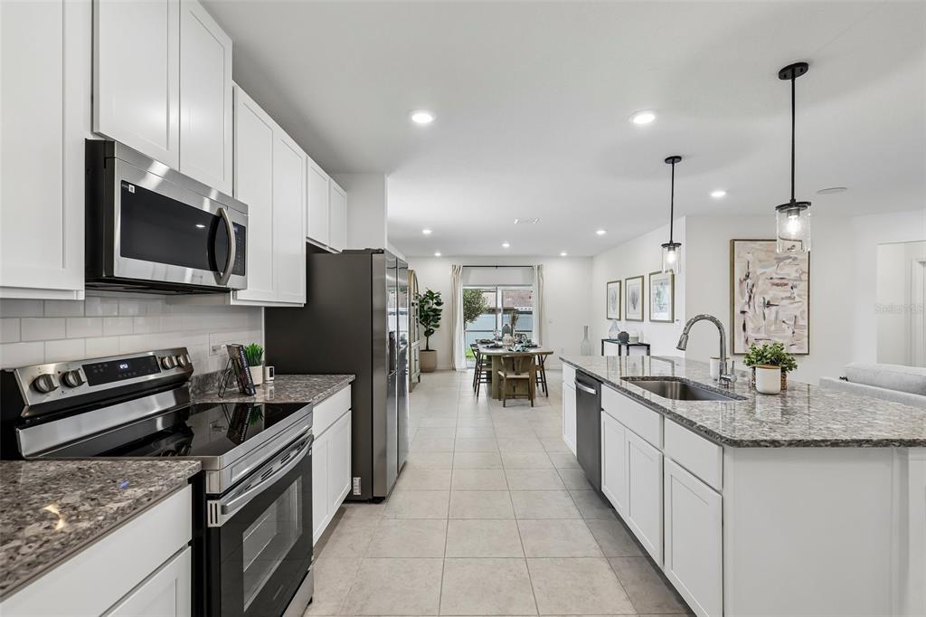 A modern kitchen with white cabinets, granite countertops, and stainless steel appliances opens to a dining area — 5955 LYON ROAD, SPRING HILL, FL